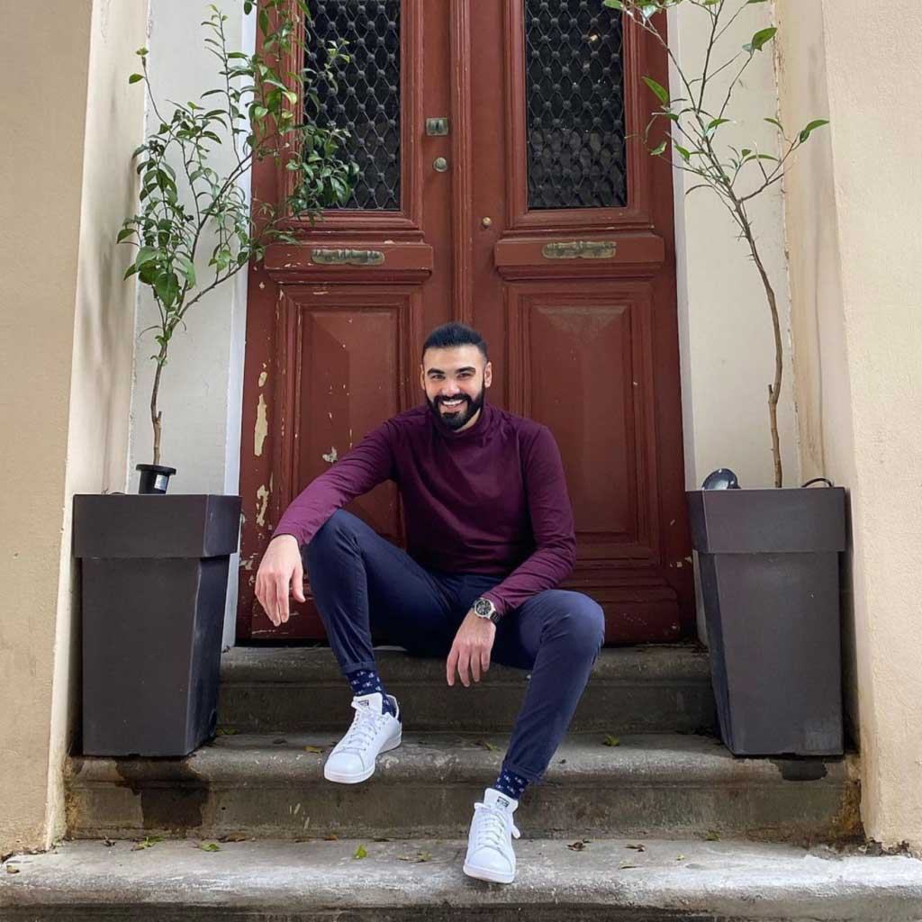 Theodoros Kalotinis smiles, sitting on a stoop in front of a doorway