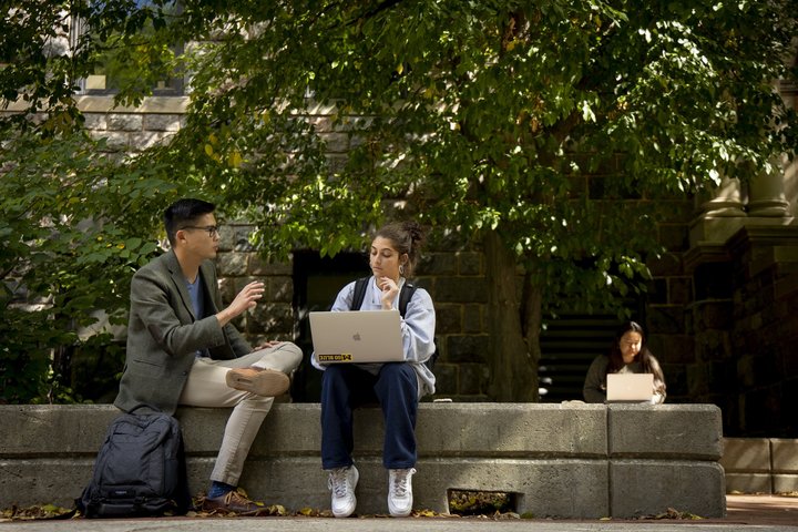 Faculty gesturing as they speak to a student while they sit outside