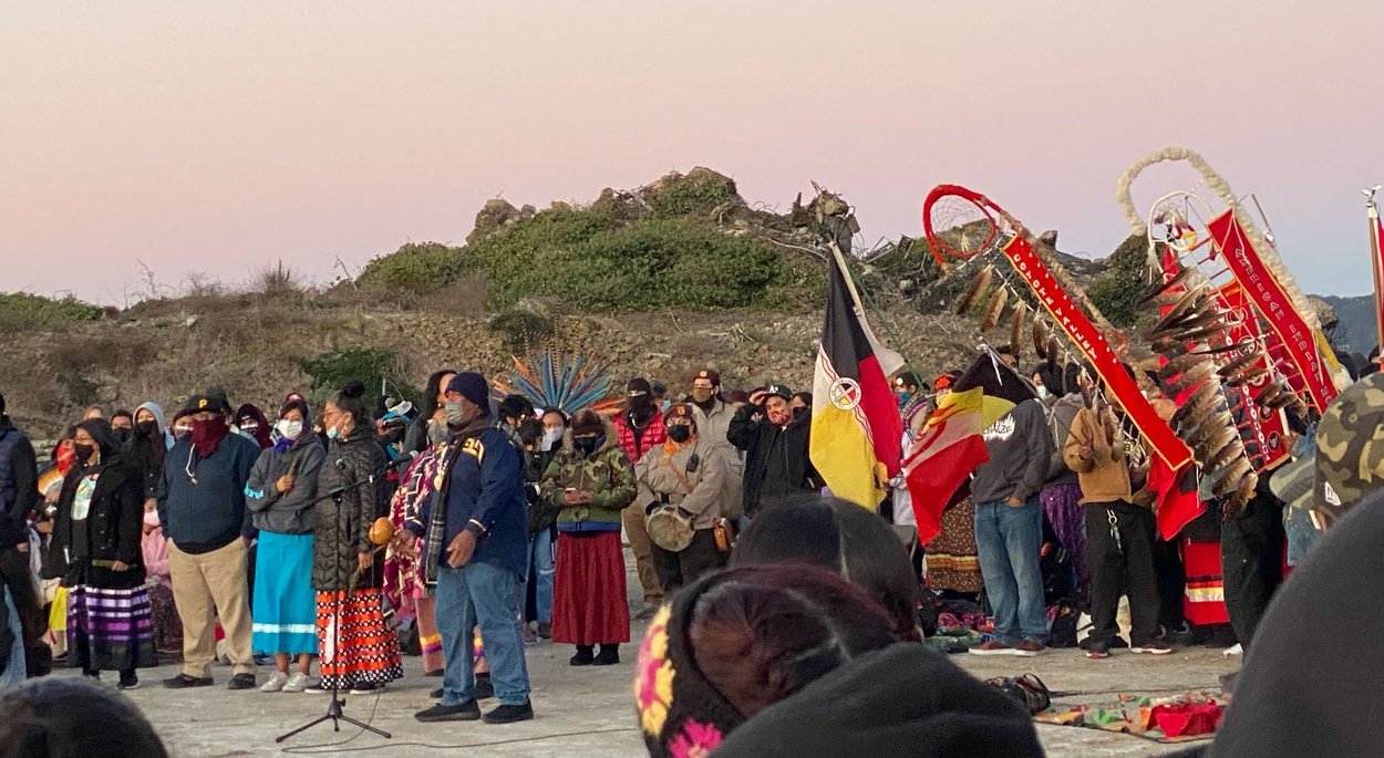A crowd of people in winter coats with colorful banners at a tribal event